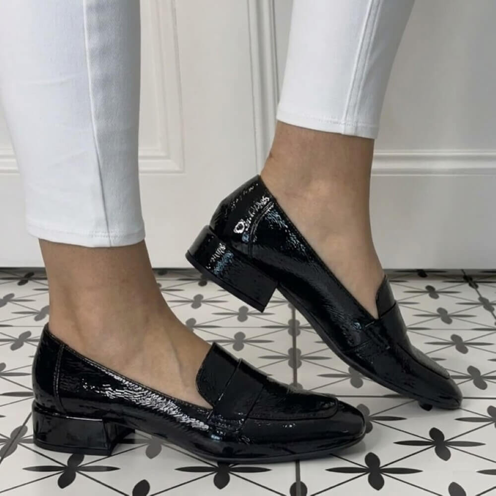 Wonders Black patent leather loafers worn with white pants on a patterned floor.