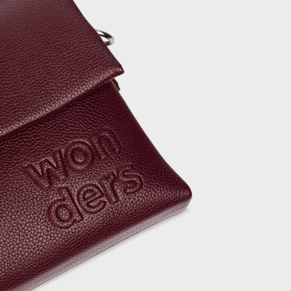 burgundy crossbody with 'wonders' branding on a light grey background