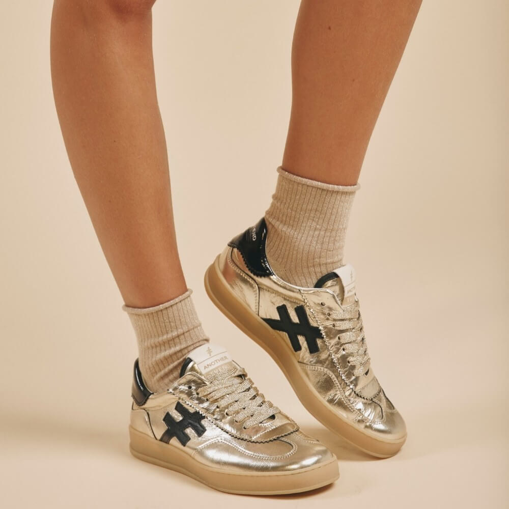 Silver sneakers with black logo worn with beige socks on a beige background