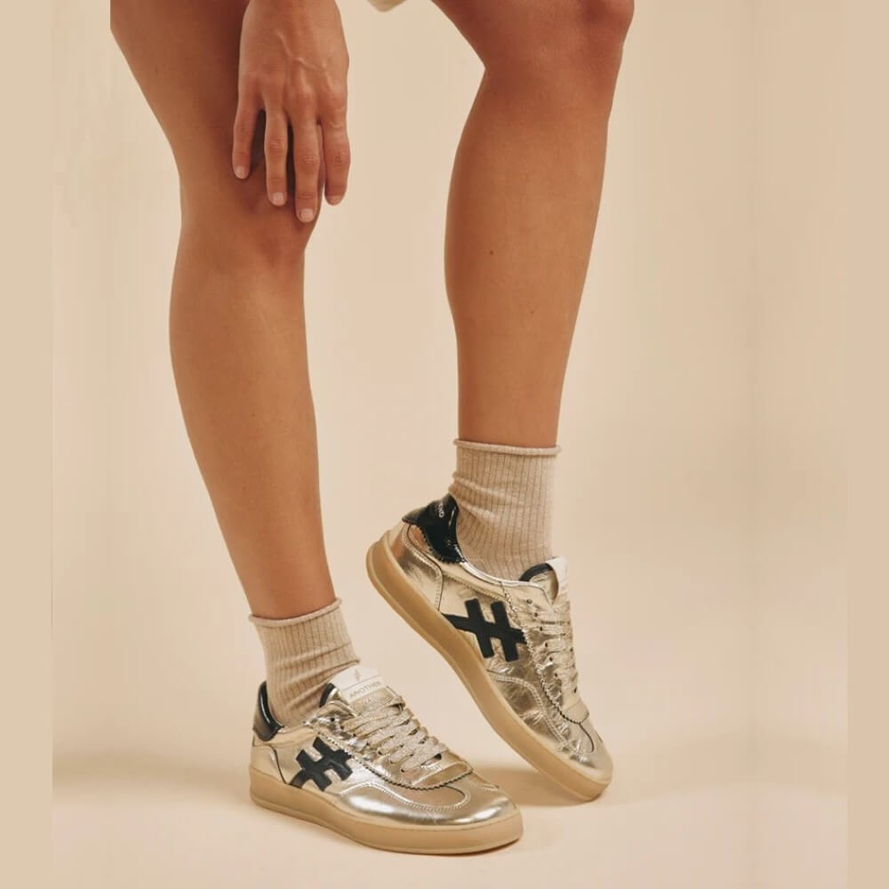 Silver sneakers with black logo worn with beige socks on a beige background