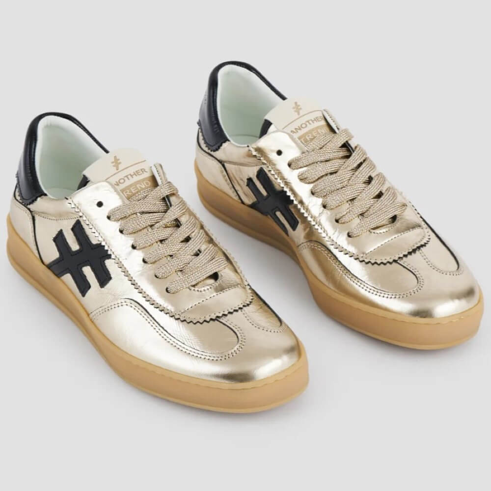 Pair of gold sneakers with black accents on a light gray background