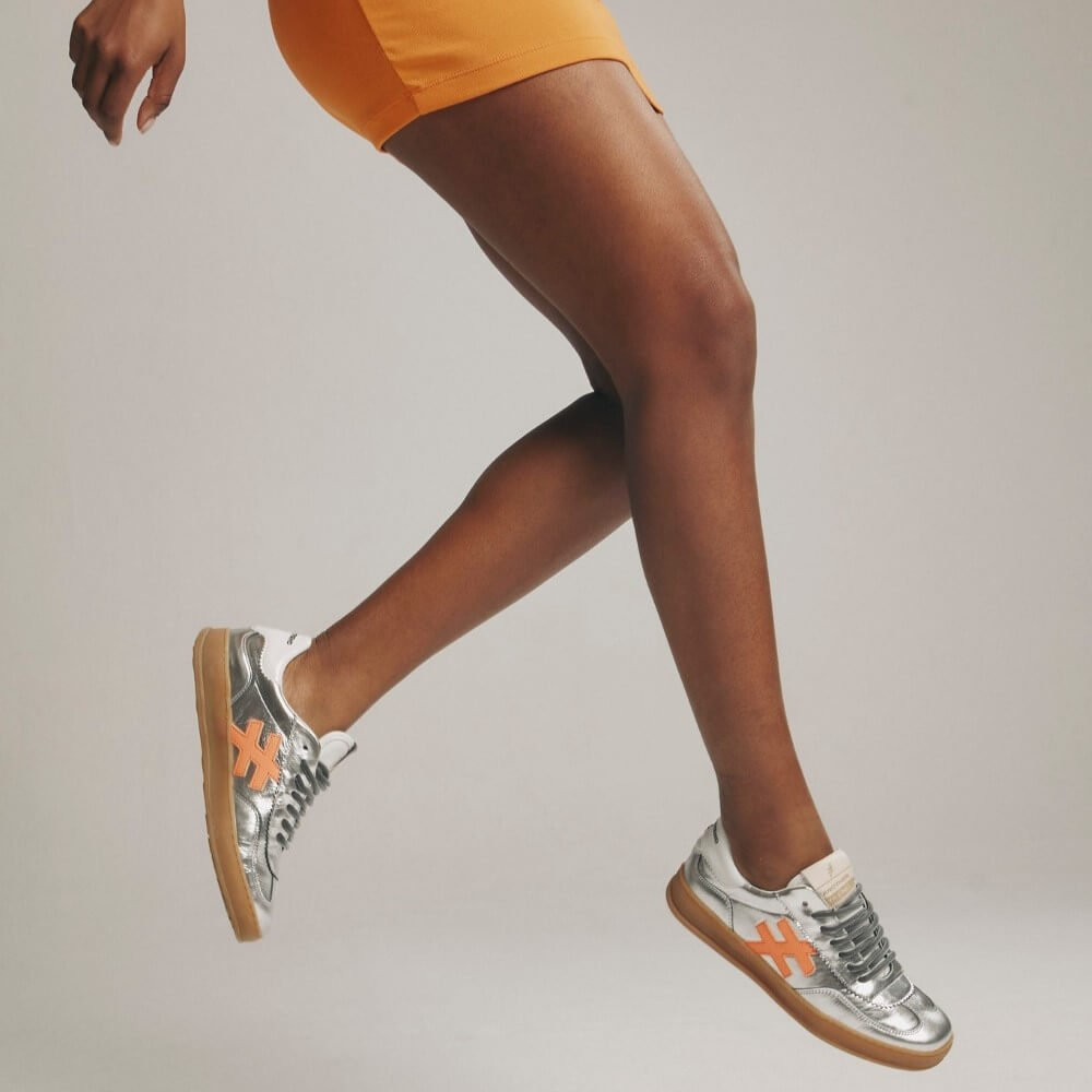 Person wearing silver sneakers with orange accents on a plain background
