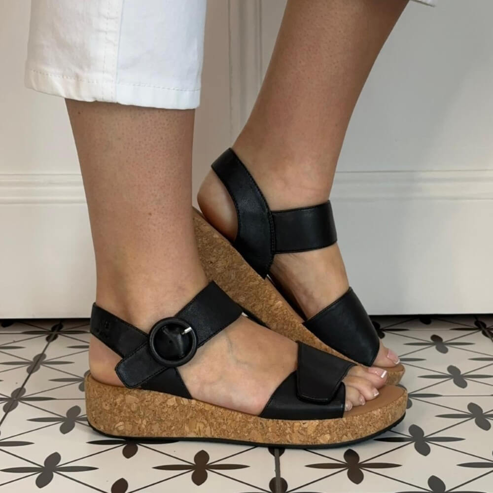 Josef Seibel Black leather sandals with cork sole worn by a person on a patterned floor.