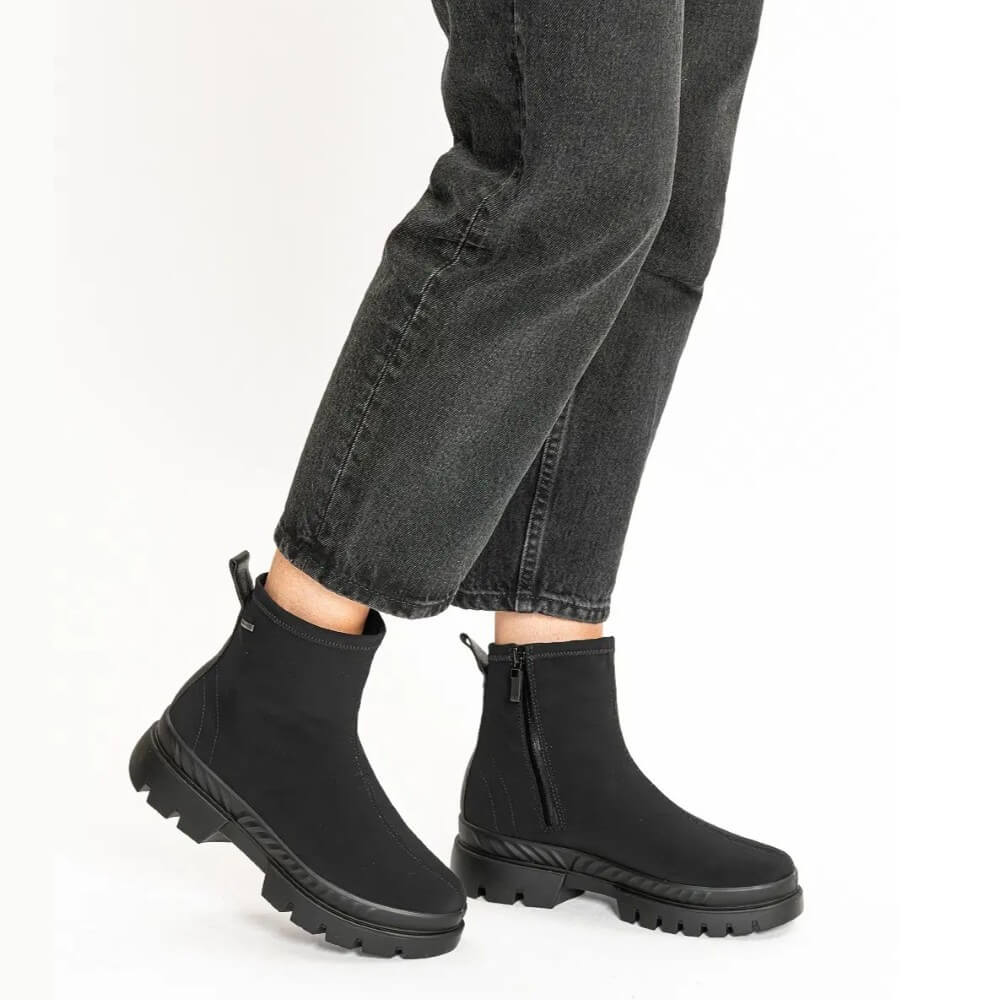 A video of a person wearing a pair of Ara Gore-Tex black ankle boots with chunky lug soles and side zippers, with black jeans