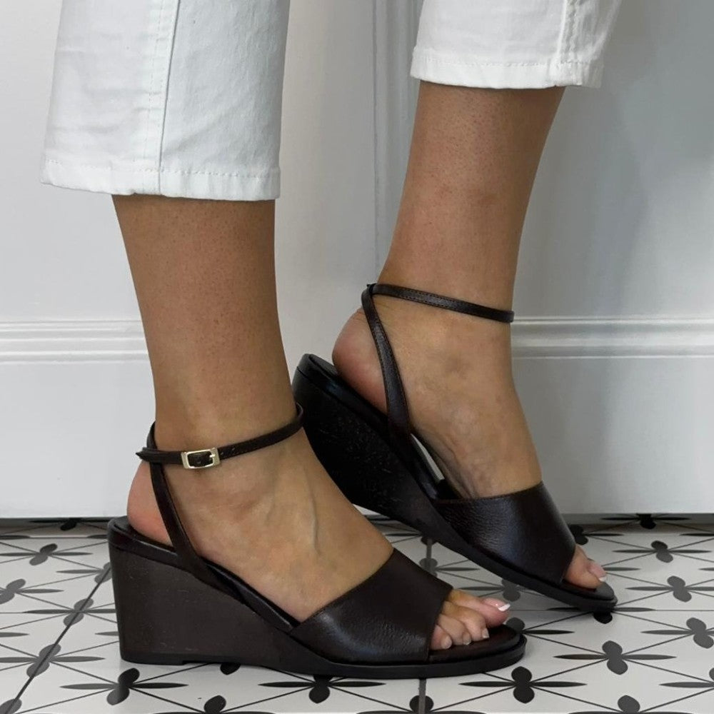 Angel Alarcon Testa Brown wedge sandals worn with white pants on a patterned floor.