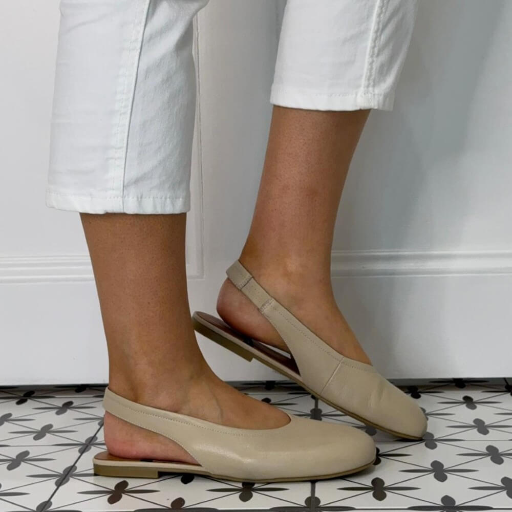 Angel Alarcon Beige flat shoes worn with white pants on a patterned floor.