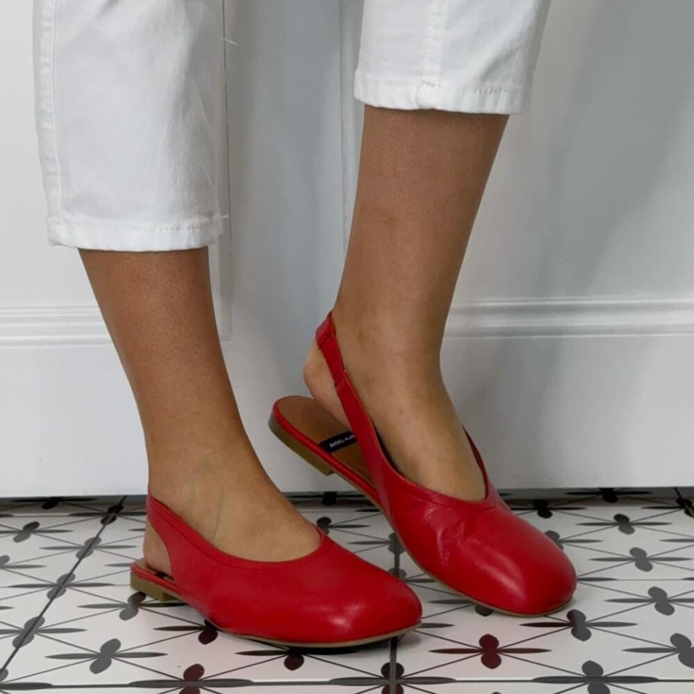 Angel Alarcon Red slingback flats worn with white pants on a patterned floor.