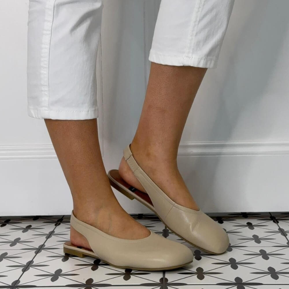 Angel Alarcon Beige flat shoes worn with white pants on a patterned floor.