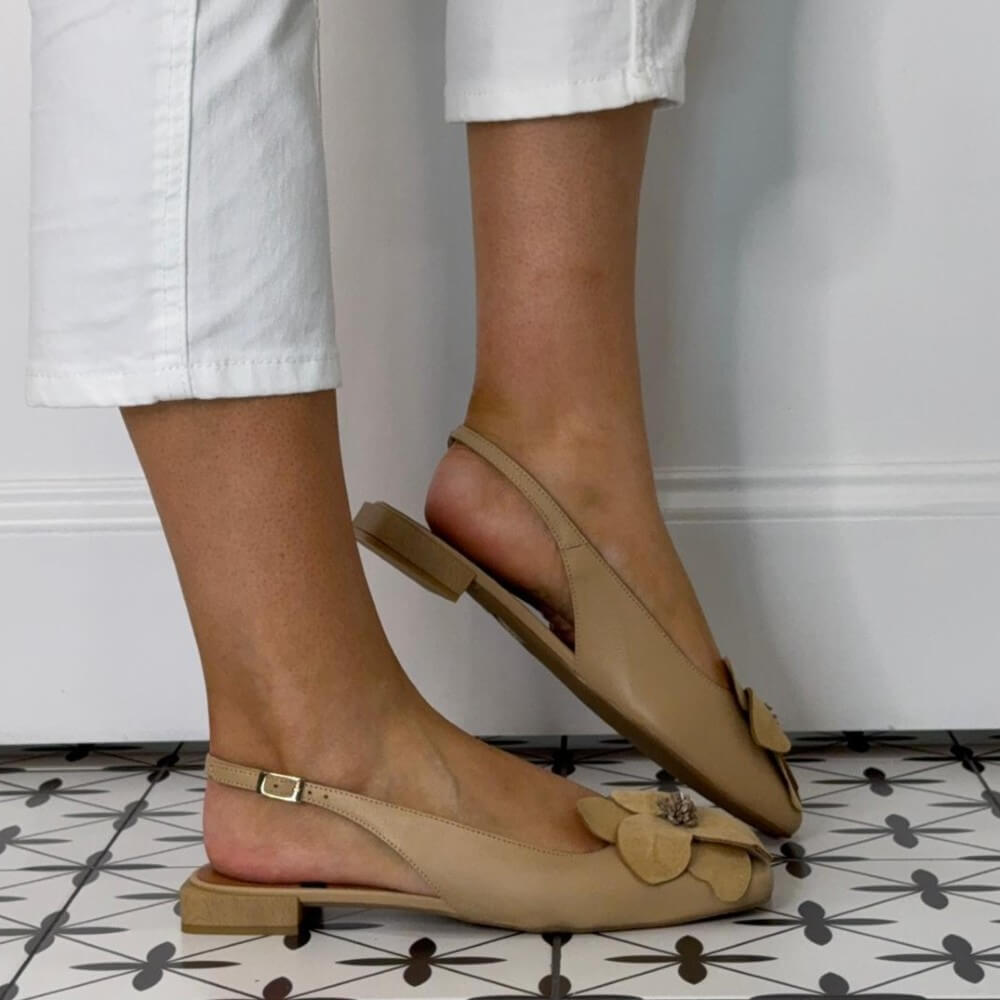 Angel Alarcon Beige flats with a flower worn with white pants on a patterned floor.