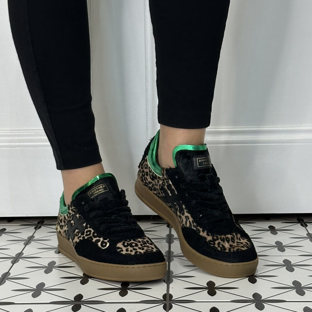Another Trend sneakers in Black, Leopard Print and green worn with black jeans on a tiled floor