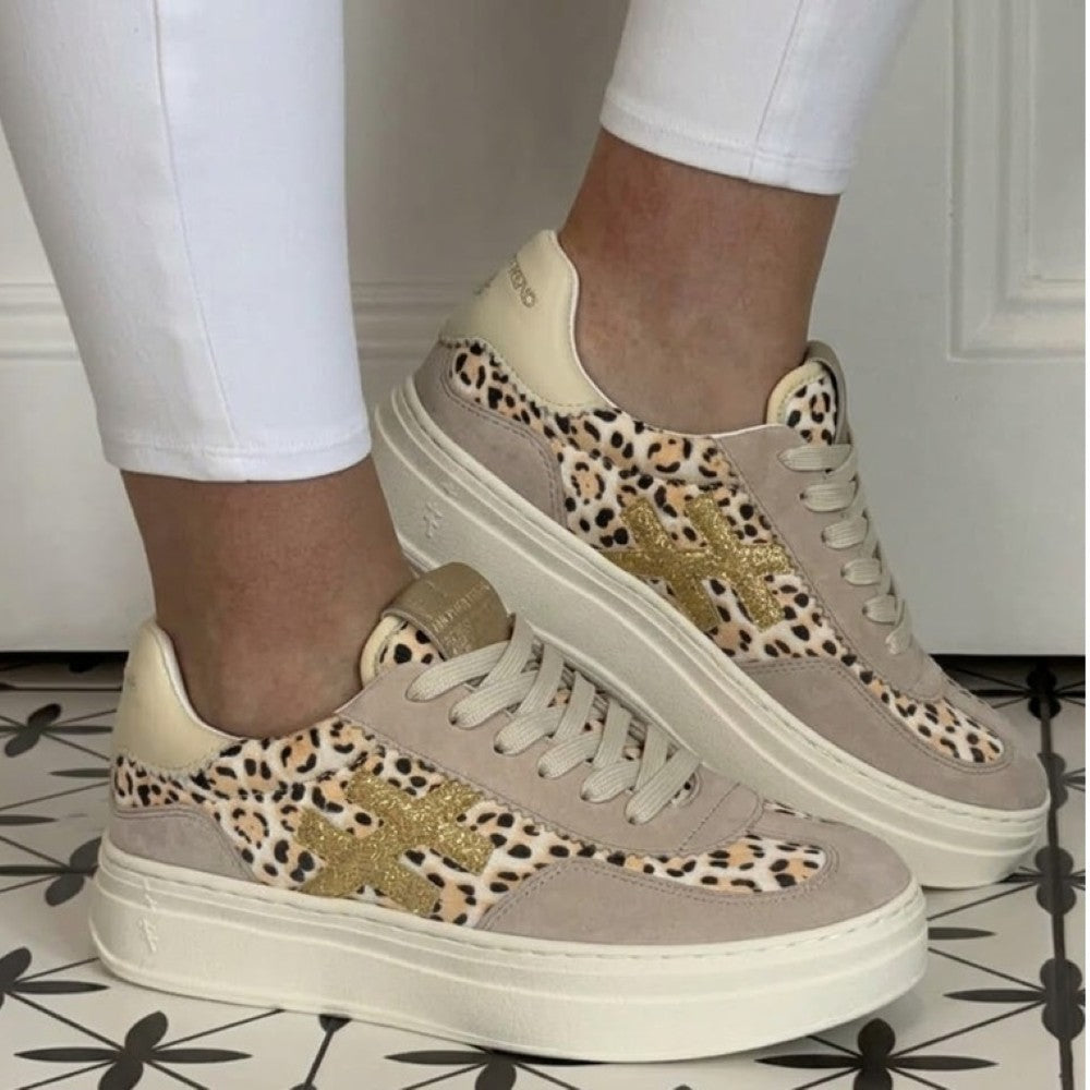 Another Trend Leopard print sneakers with gold accents worn indoors on a patterned floor.