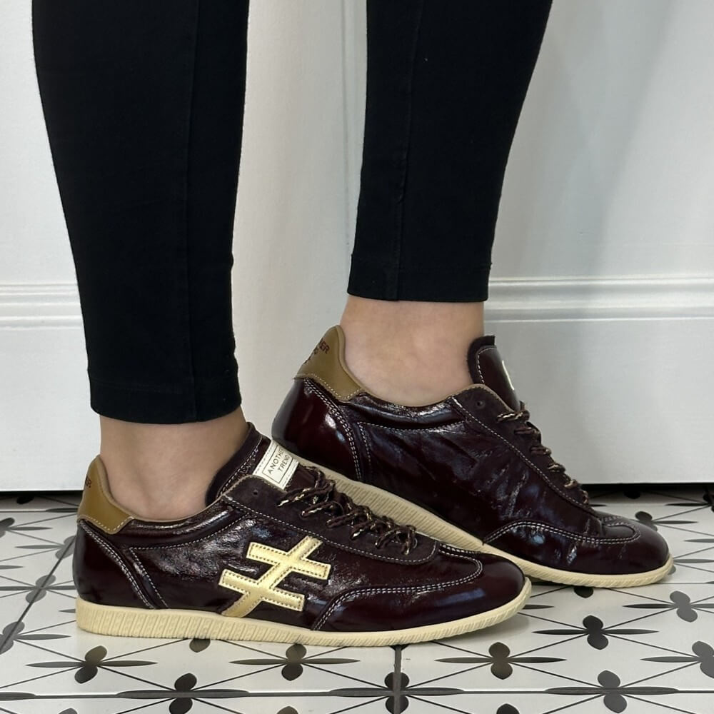 Another Trend Wine Patent Leather Trainers worn with black jeans on a tiled floor 