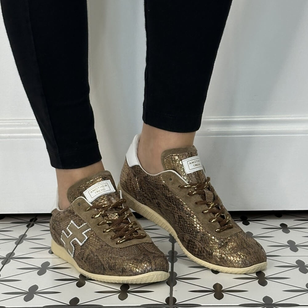 Another Trend A078 Trainers Light Bronze Snake Effect Leather worn with black jeans on a tiled floor