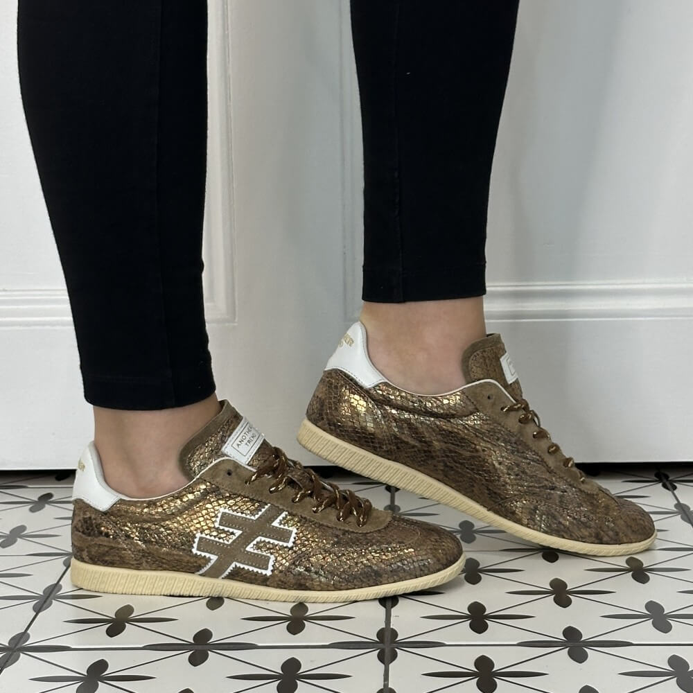 Another Trend A078 Trainers Light Bronze Snake Effect Leather worn with black jeans on a tiled floor