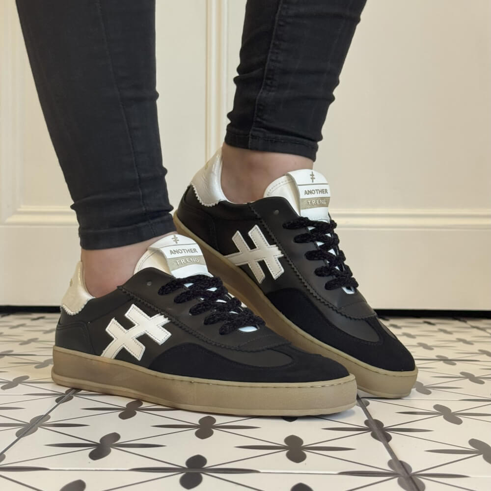 Black sneakers with white accents worn indoors on a patterned floor. Another Trend Iconic Leather Sneakers A032-Black & White