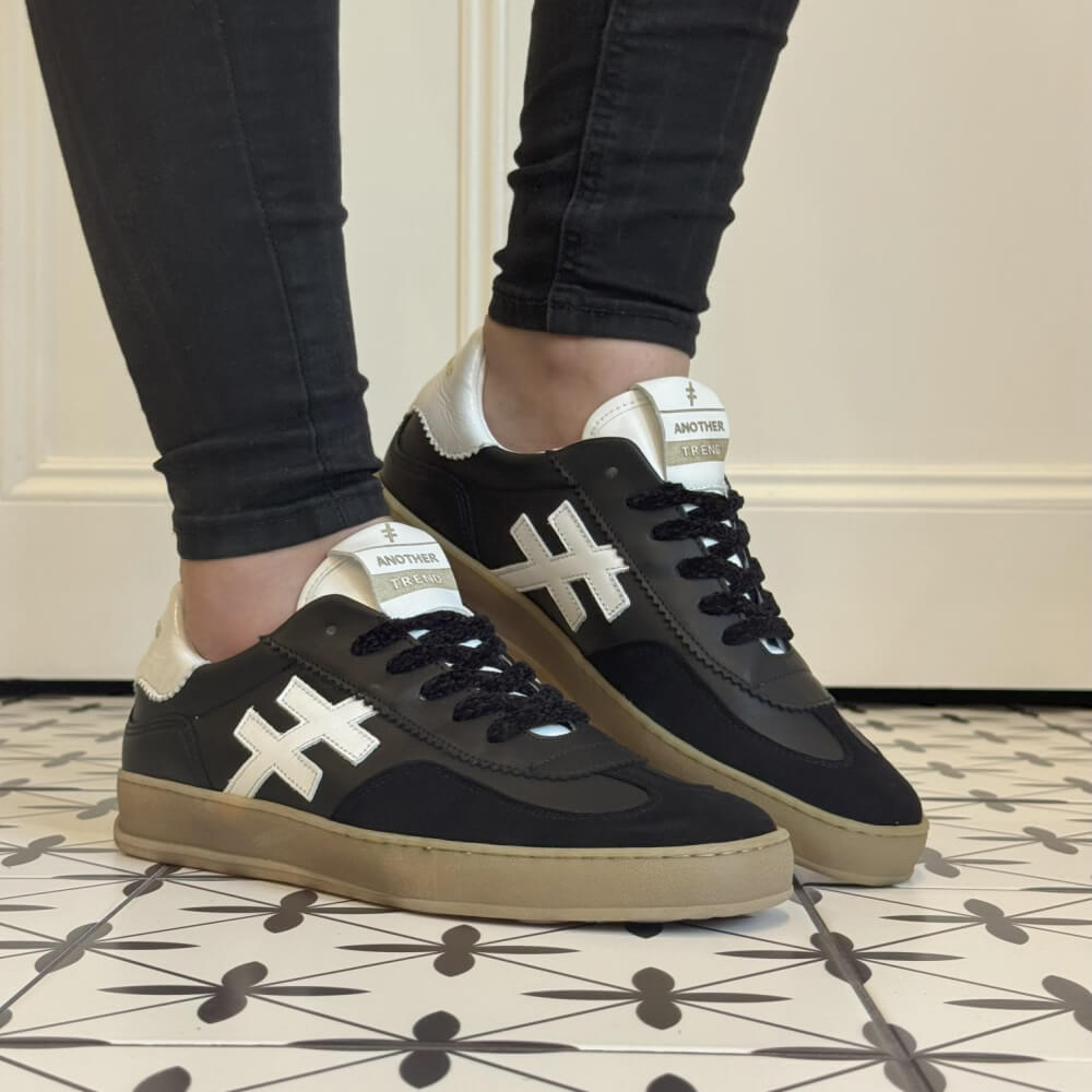 Black sneakers with white accents worn indoors on a patterned floor. Another Trend Iconic Leather Sneakers A032-Black & White