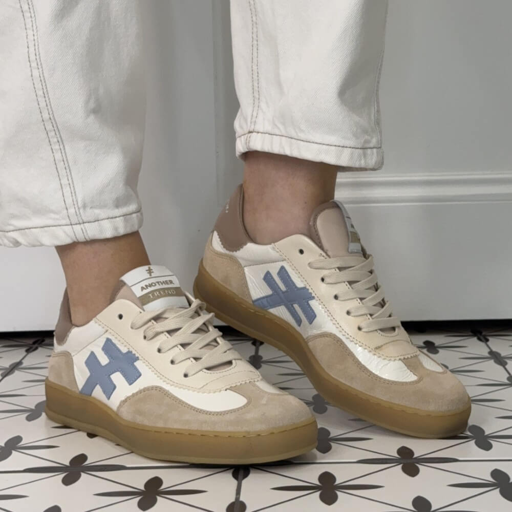 another trend Beige sneakers with blue geometric designs worn indoors on a patterned floor.