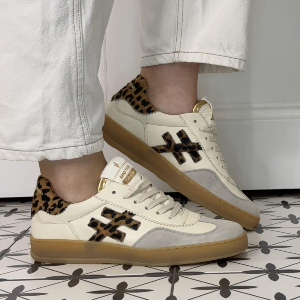 White sneakers with leopard print accents worn by a person on a patterned floor.