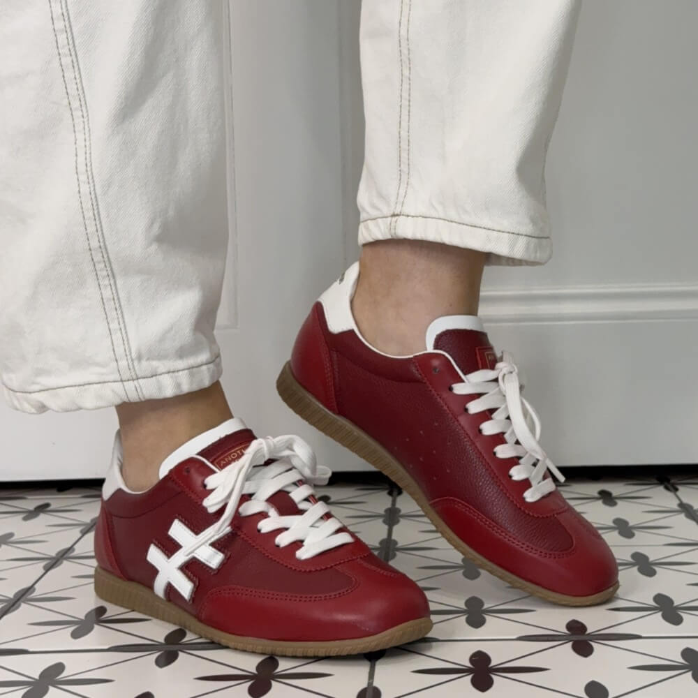 Red sneakers with white laces worn indoors on a patterned floor.