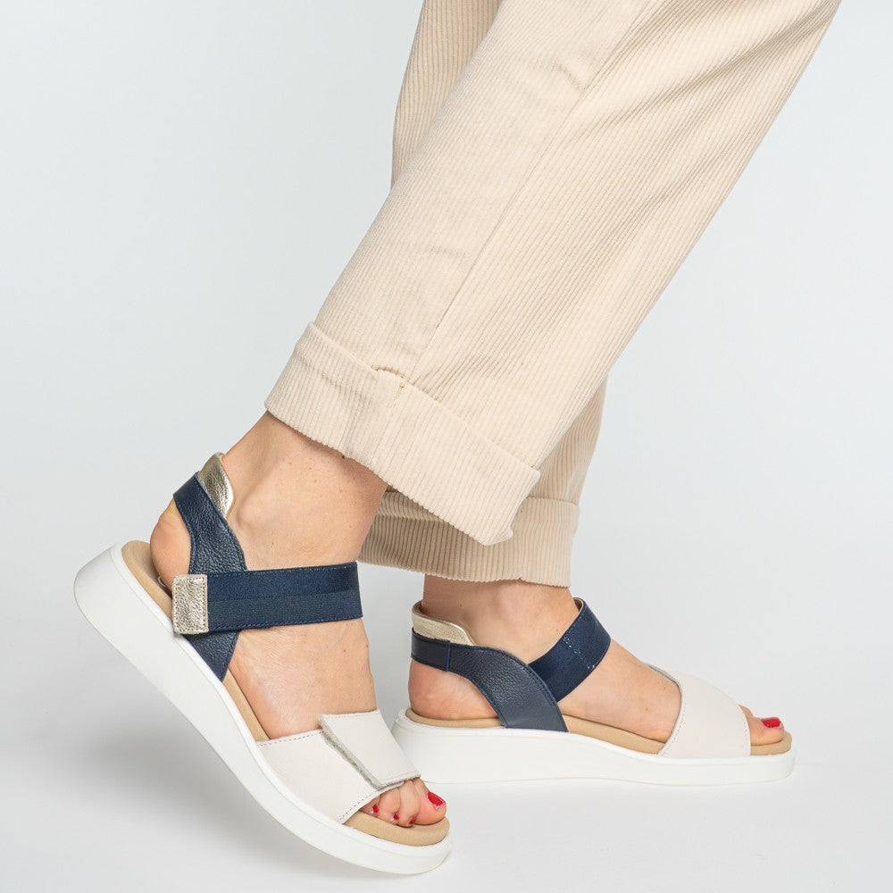Ara White and navy sandals worn with beige pants on a light grey background