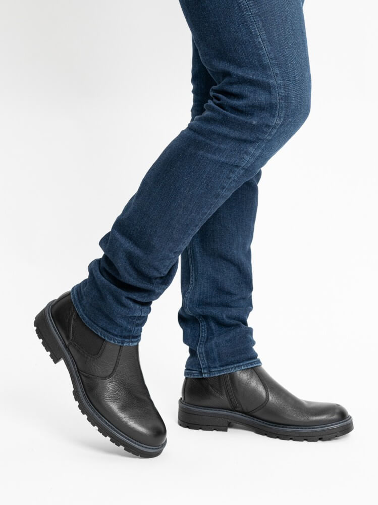 Person wearing black leather boots and blue jeans on a white background