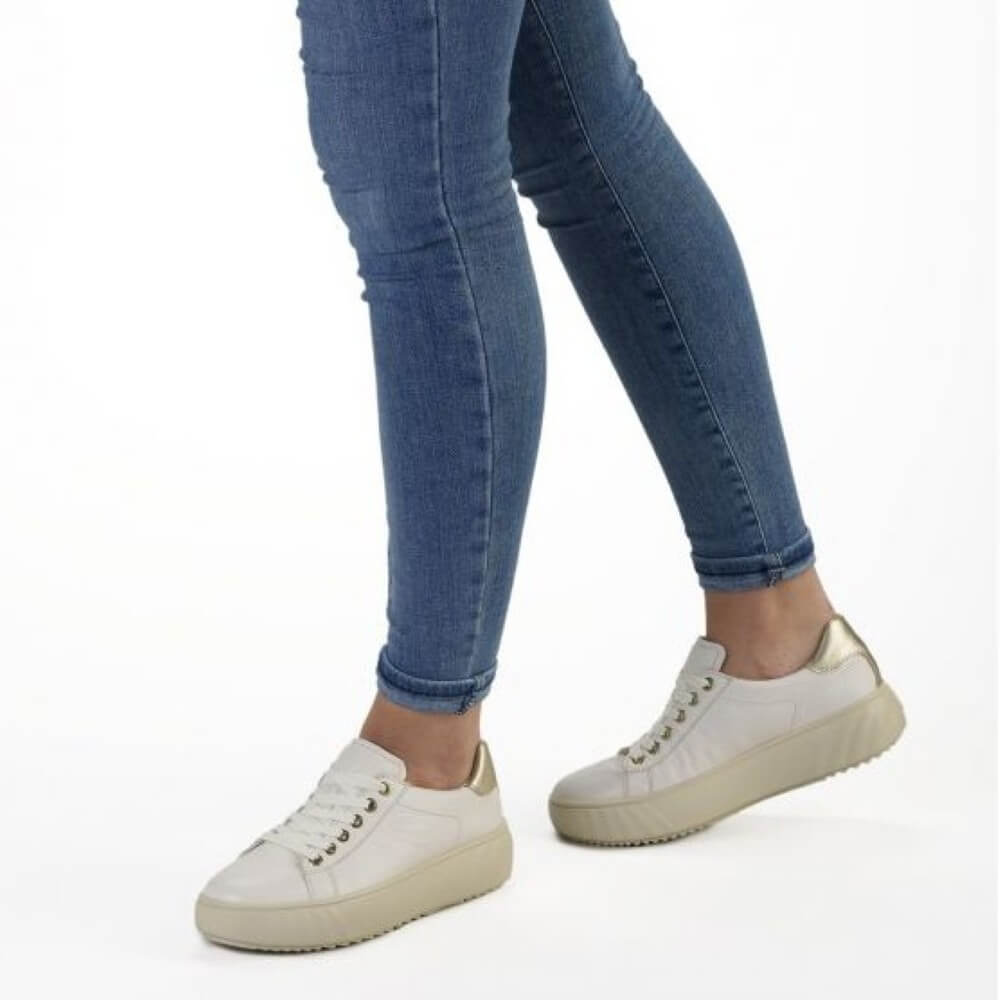 cream leather sneakers worn with blue jeans on a white background