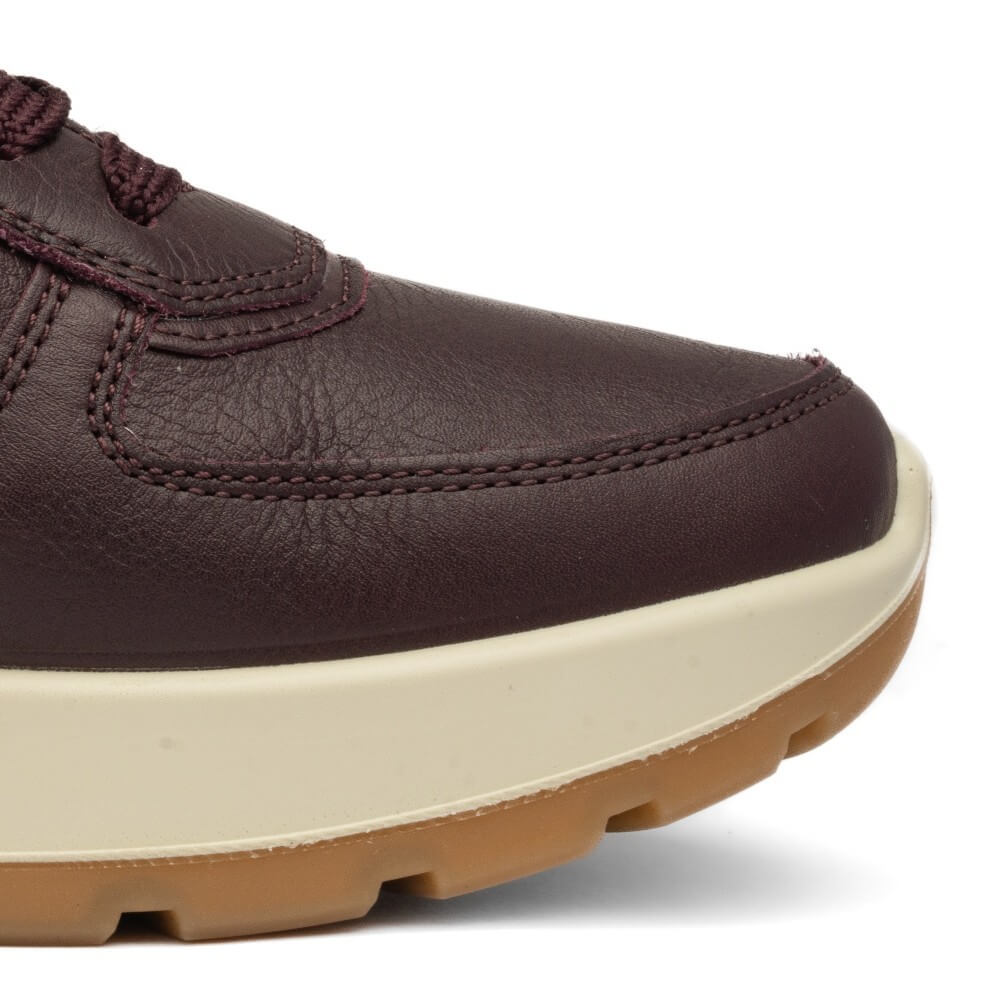 Close-up of a dark brown leather sneaker showing the toe cap, side stitching, cream midsole, and gum outsole on a white background.