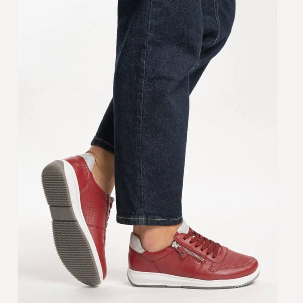 Red sneakers with white soles worn with dark jeans on a light gray background