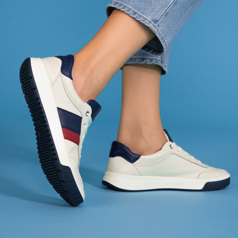 White sneakers with navy and red accents worn by a person on a blue background