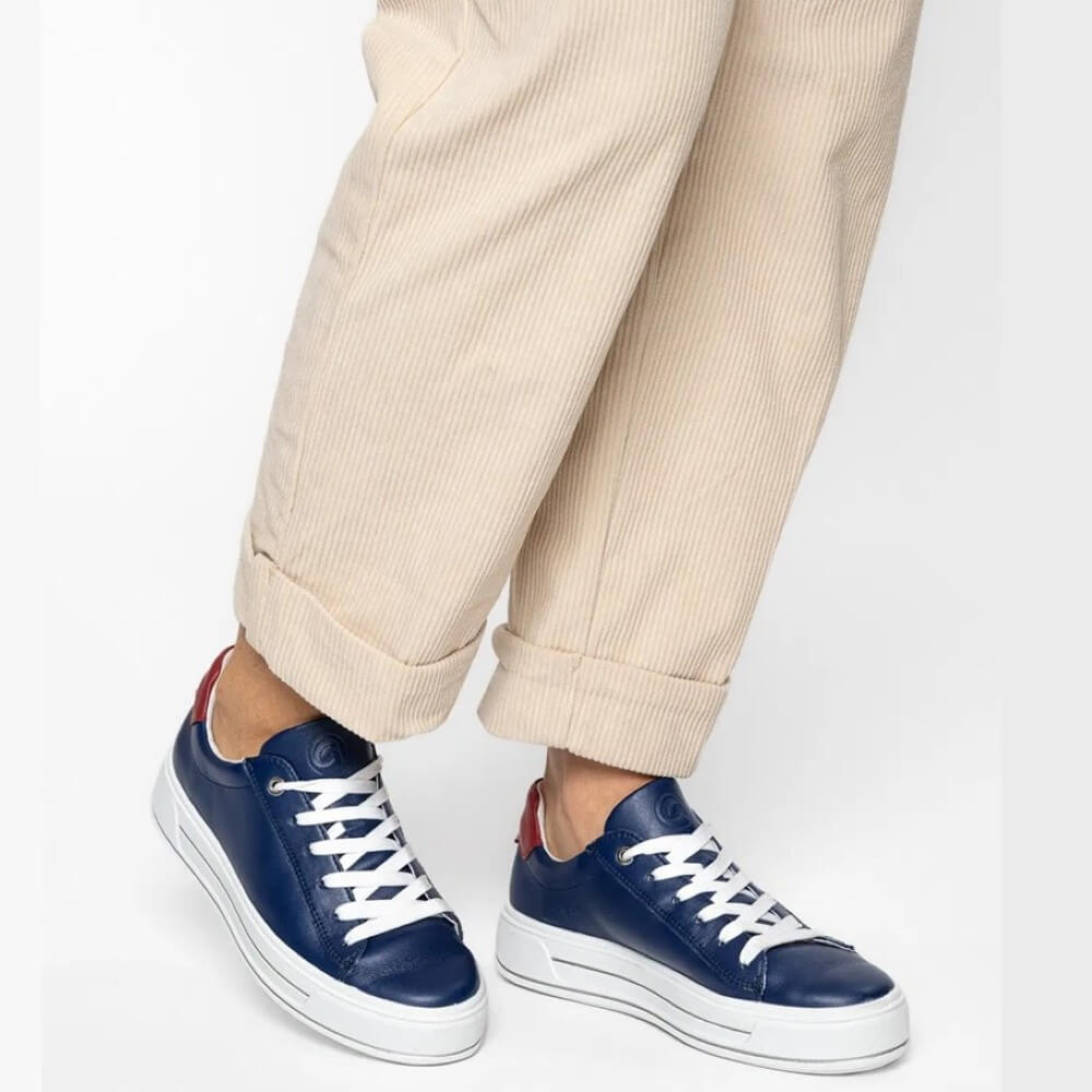 Navy sneakers with white soles worn with beige pants on a light gray background