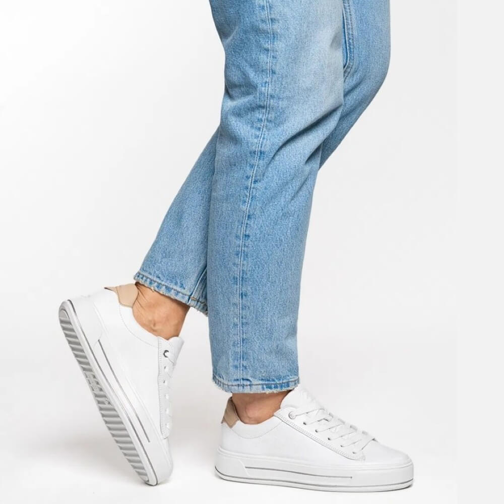 White sneakers worn with light blue jeans on a white background