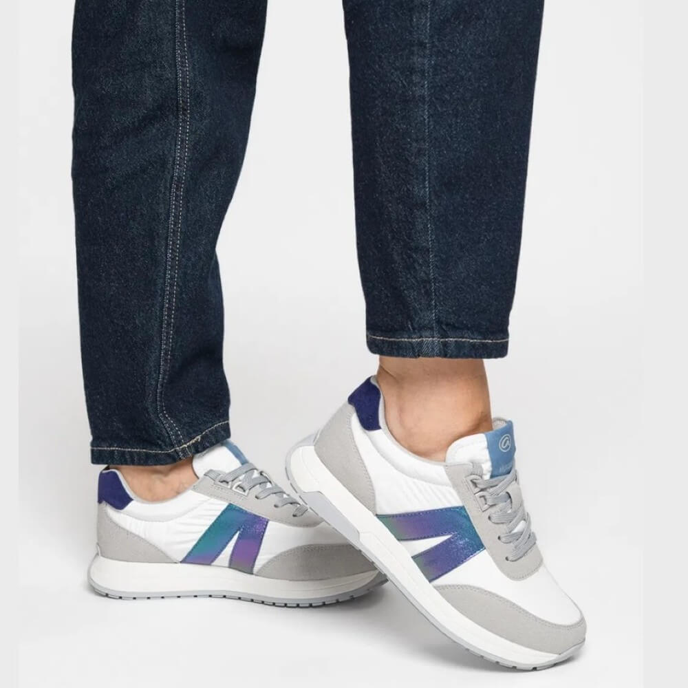 White sneakers with blue and beige accents worn with dark jeans on a light gray background