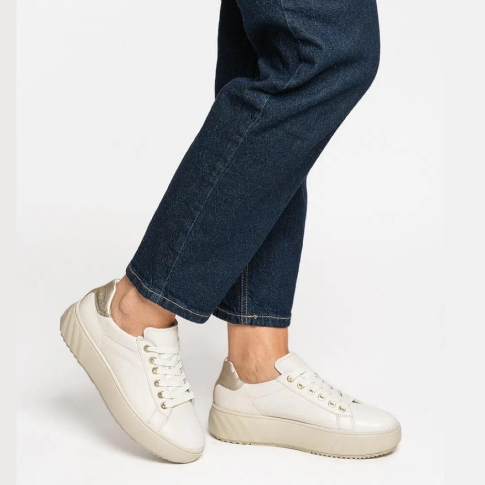 Cream leather sneakers worn with blue jeans on a white background