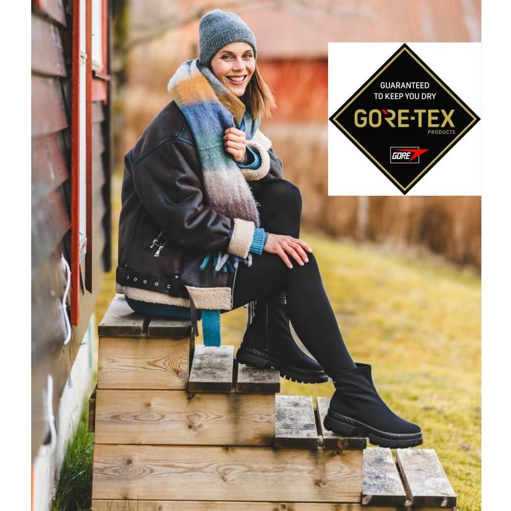 Person sitting on wooden steps wearing Gore-Tex boots with the brand logo displayed.