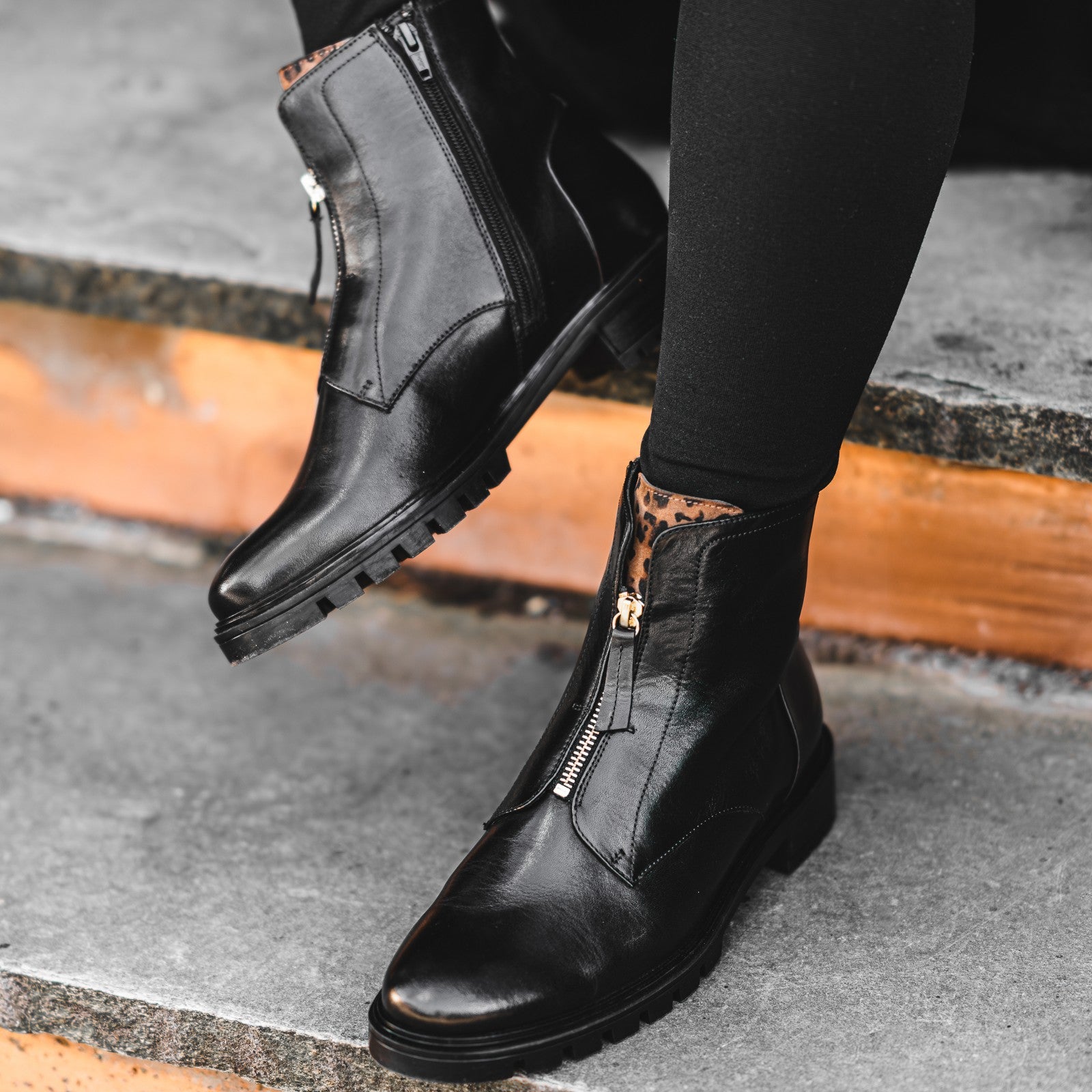 Black leather boots with zippers worn by a person on a concrete surface. Ara Tulsa ST Ankle Boot 12-29520 ARA-BLACK