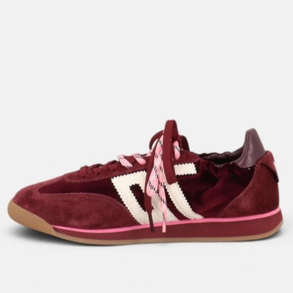 A single low-top sneaker in burgundy suede with a white embroidered side stripe, pink laces, and a gum sole, shown from a side profile on a light gray background.