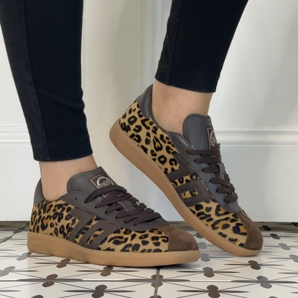 A pair of Back 70 Retro sneakers with a leopard print pattern on the uppers, dark brown leather overlays, and gum soles, shown being worn with black pants.