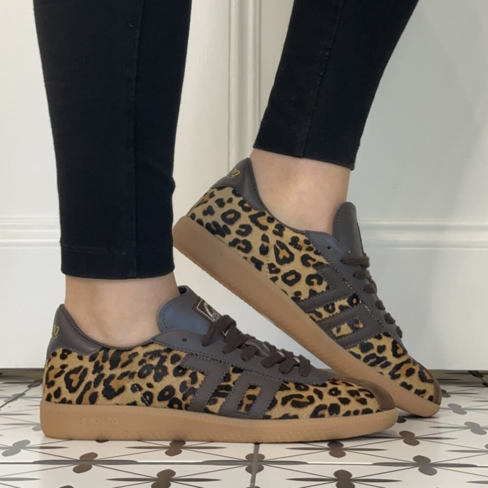 A pair of Back 70 Retro sneakers with a leopard print pattern on the uppers, dark brown leather overlays, and gum soles, shown being worn with black pants.