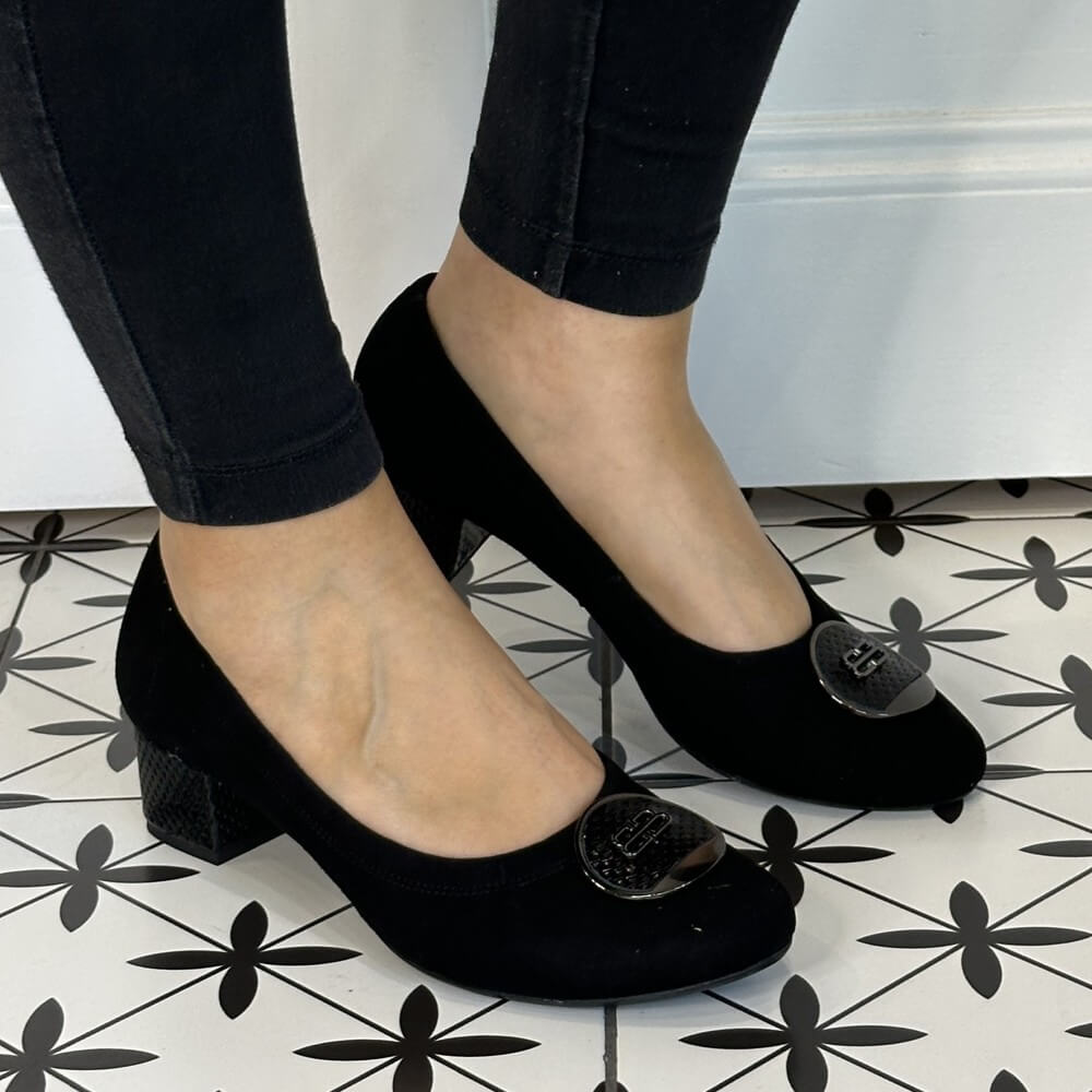 Black high-heeled shoes with decorative buttons worn by a person on a patterned floor. Black low heel shoes worn with black pants on a patterned floor. Bioeco 6861 Low Block Heel Black Suede court shoes