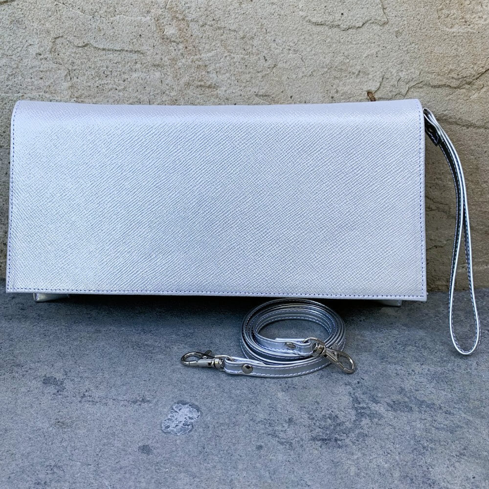 silver textured clutch bag with a strap on a concrete surface.