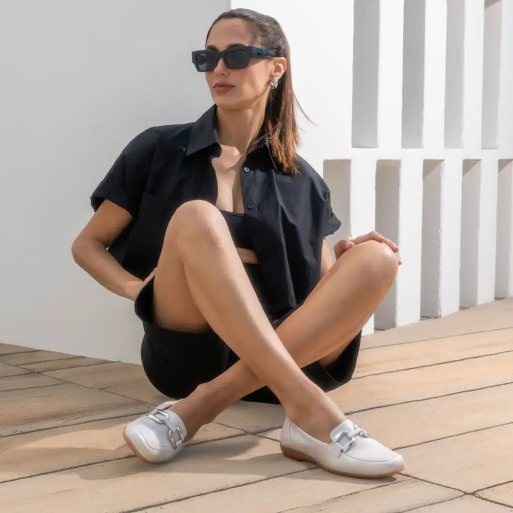 Woman in black outfit with white loafers sitting on a wooden floor.