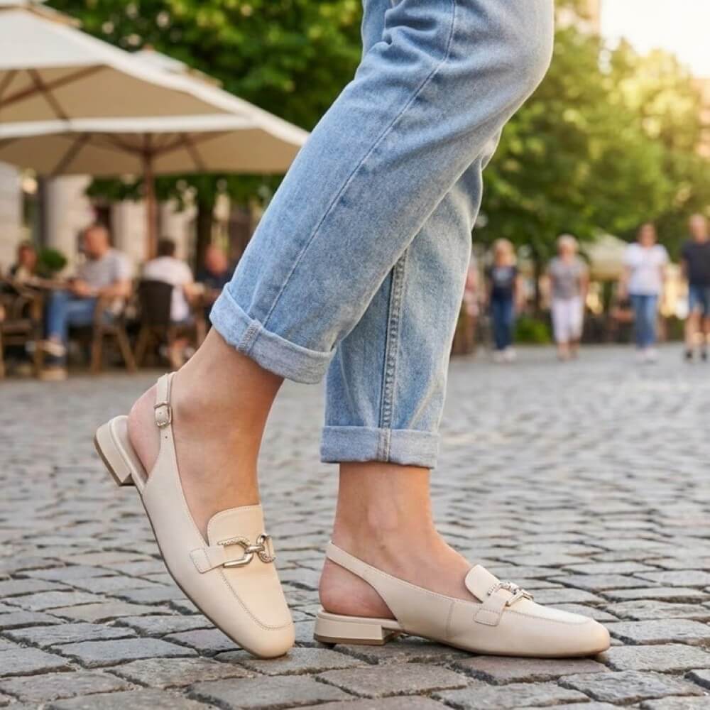 Person wearing Caprice 29400 beige loafers and blue jeans on a cobblestone street with blurred background
