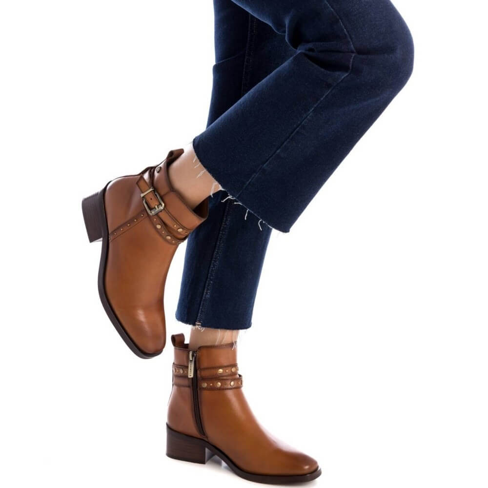Brown ankle boots with buckles worn with blue jeans on a white background