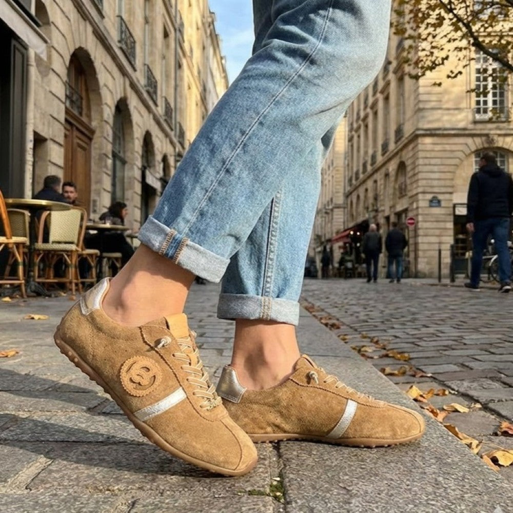Person wearing tan sneakers with silver accents on a city street.