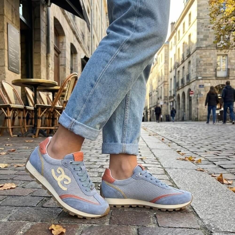 Person wearing Carmela blue sneakers with orange accents on a city street.