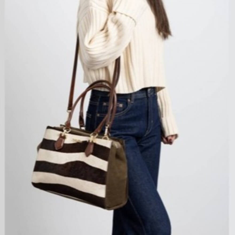 Person wearing a striped handbag, white sweater, and blue jeans on a light gray background