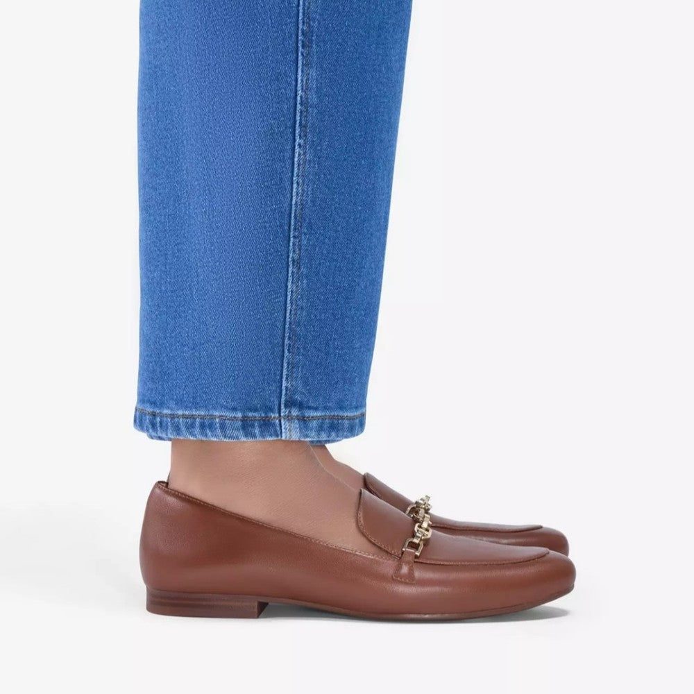 Clarks Brown loafers with gold accents worn with blue jeans on a white background