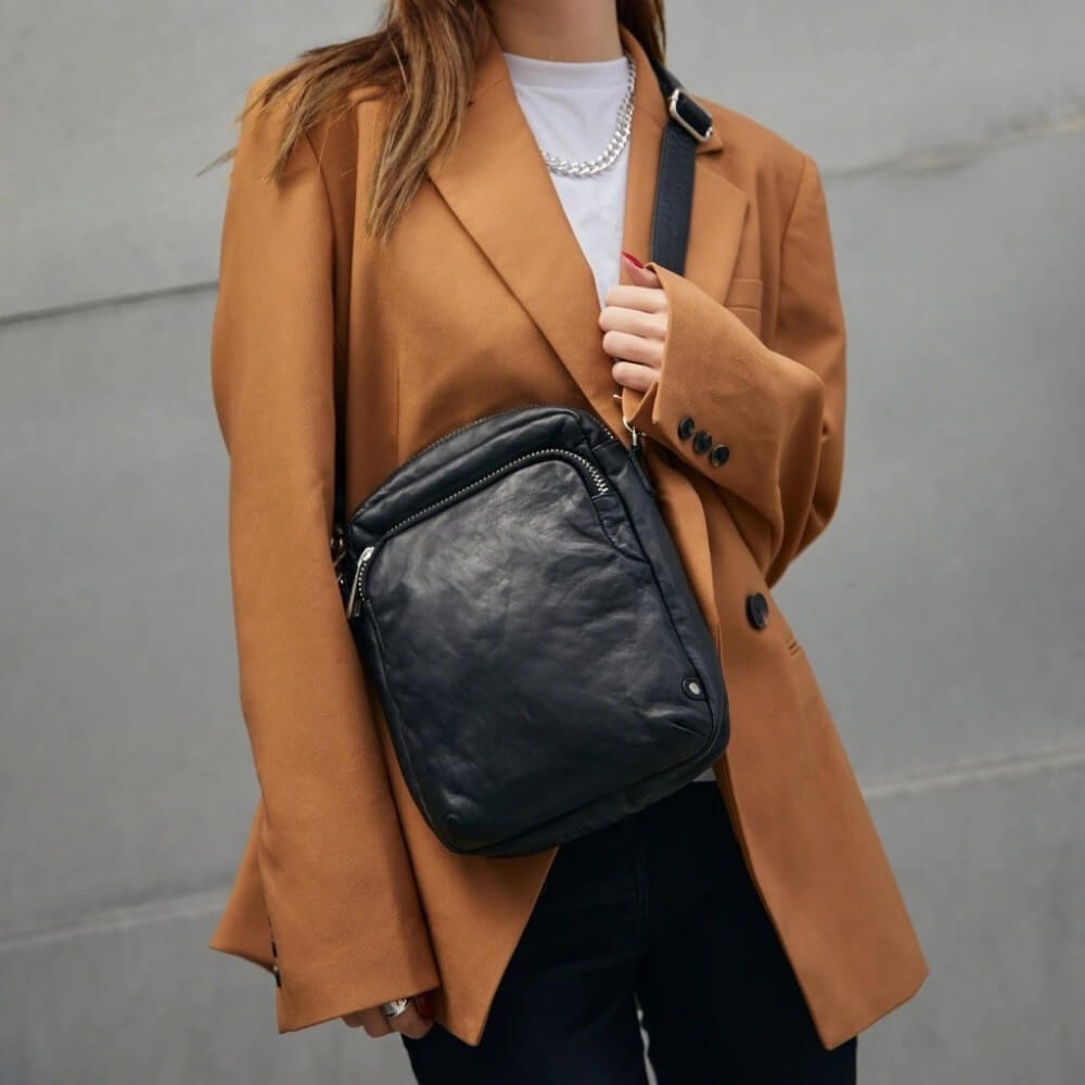 Person wearing a Depeche Black leather crossbody bag with a camel coat