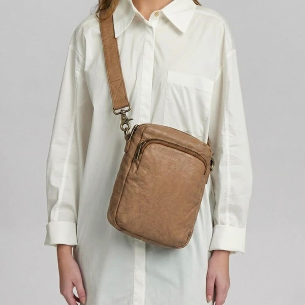 Person wearing a depeche brown crossbody bag with a plain background