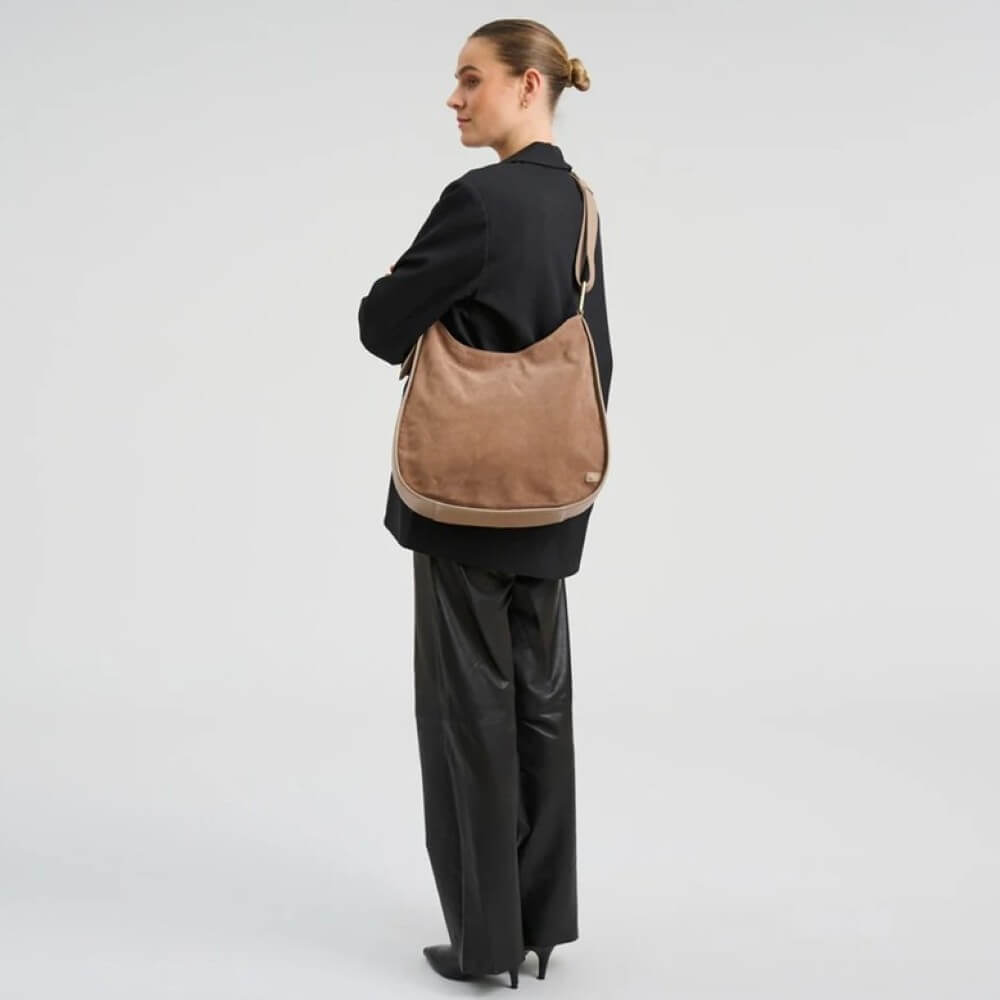 Woman carrying a Depeche brown leather bag on a plain background